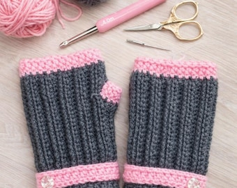 May include: A pair of grey and pink crochet fingerless gloves. The gloves feature a ribbed design with pink cuffs and a decorative button. The image also shows crochet supplies, including yarn, a crochet hook, and scissors. The text at the top says "Crochet Fingerless Gloves Pattern".