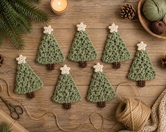 May include: A set of six crocheted Christmas tree ornaments in sage green with small cream-colored stars at the top and brown trunks. Each triangular tree features a textured stitch pattern and is arranged on a wooden surface with craft supplies.