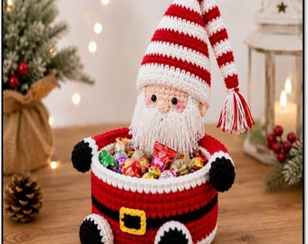 May include: A crocheted Santa Claus basket featuring a red and white striped hat with a tassel, a white beard, and a red base with a black belt and yellow buckle. The basket is filled with various colourful wrapped candies and chocolates.