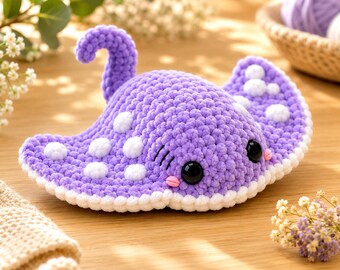 May include: A purple crochet stingray plush toy featuring a textured yarn surface, white polka dot patterns on its wings, a curved tail, large black plastic safety eyes, and small pink stitched cheeks, finished with a white border along the edges.