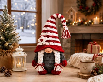 May include: A crocheted gnome figurine featuring a tall, floppy hat with red and white horizontal stripes, a white flower accent, and a tassel. The gnome has a round beige nose, two long white braided pigtails, a dark grey body, and red mittens.