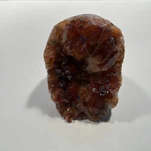 Könnte beinhalten: Eine tief bernsteinfarbene und braune Kristallgruppe mit rauer, gezackter Oberfläche. Das Mineralexemplar weist zahlreiche kleine, spitze, durchscheinende Punkte auf, die das Licht einfangen und ein strukturiertes Aussehen verleihen.