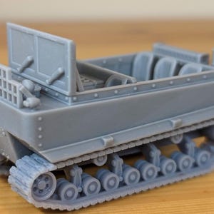 May include: A gray model of a tracked vehicle, possibly a tank or tractor. The vehicle has a detailed interior with seats and a steering wheel. The tracks are visible, and the overall design suggests a miniature replica of a military or industrial machine.
