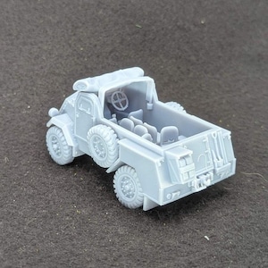 Puede incluir: Un camión militar de juguete gris claro con seis ruedas, un volante y una zona de carga trasera. El camión tiene un diseño detallado, que incluye un parabrisas delantero, faros y una rueda de repuesto. El juguete es de plástico y está sobre una superficie gris.