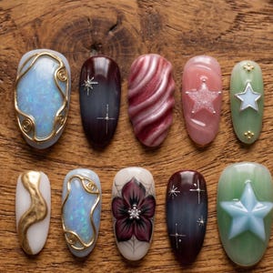 May include: A collection of ten artificial nails with various designs. The nails feature colors like blue, white, gold, red, and pink. Some nails have star and floral accents, while others have abstract patterns and gold wire detailing. The nails are arranged on a wooden surface.