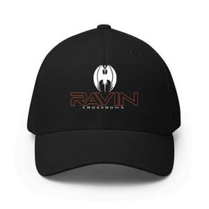 May include: Black baseball cap with the text "RAVIN CROSSBOWS" in orange and white. The cap features a white graphic of a stylized bird or wing design above the text. The cap has a curved brim and a structured fit.