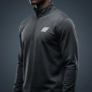 以下が含まれることがあります： チャコールグレーの長袖アスレチックシャツ。モックネックとクォータージップクロージャー付き。胸元には白いロゴがあります。柔らかく通気性の良い素材で、ワークアウトや普段使いに適しています。