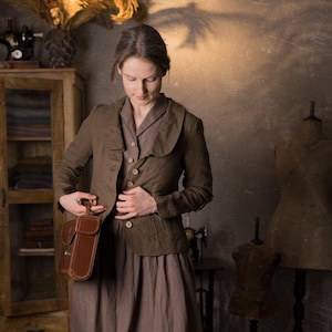 Woman wearing slim-fit mushroom brown linen jacket with button front, curved collar and long sleeves, styled over brown midi dress and holding leather bag in rustic studio, retro linen jacket by knock knock linen.