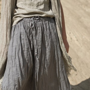 Model standing on sand wearing frost grey linen drawstring pants with loose fit, paired with matching short-sleeved top and scarf; fabric appears soft and naturally wrinkled. Keywords: linen summer pants, drawstring pants, loose fit.