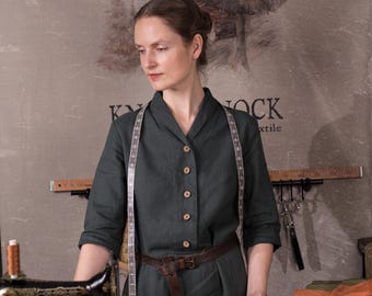 Puede incluir: Un vestido verde oscuro con botones y cinturón de cuero marrón. Una cinta métrica alrededor del cuello. Una máquina de coser vintage sobre una mesa de madera. El fondo tiene una pintura de árbol y el texto "KYNOCK textile".