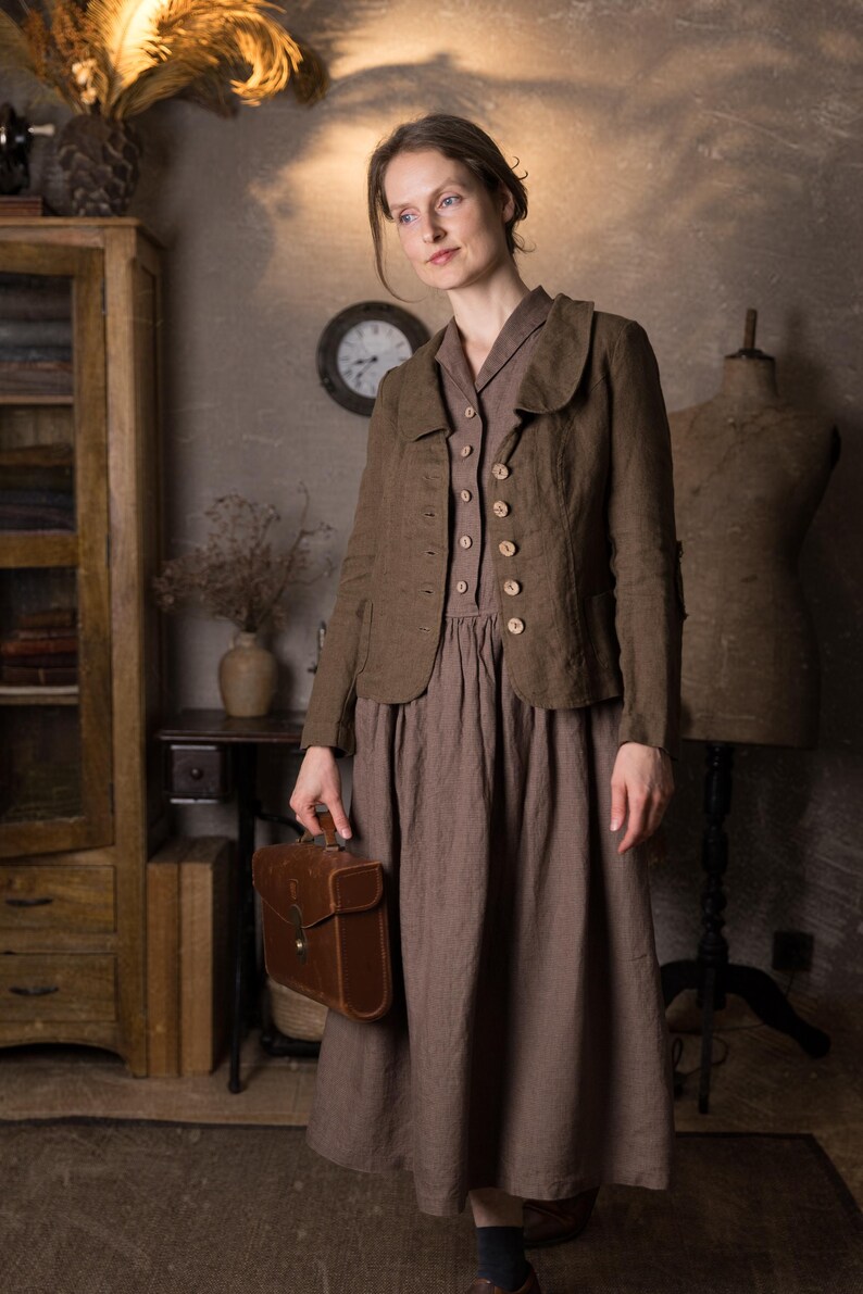 Woman in rustic studio wearing mushroom brown slim fit linen jacket with curved collar, long sleeves and button front over brown midi dress, holding brown leather briefcase, retro linen jacket by knock knock linen.