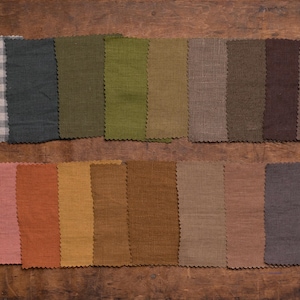 KnockKnockLinen fabric sample set—20 linen swatches in brown, green, and gray tones; solids plus gingham and houndstooth; pinked edges arranged in two rows, flat lay on a wooden surface. Fabric samples / swatch book.