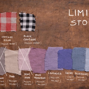 Flat lay of twelve linen fabric swatches on wood, labeled with color and weight. Top row: Cottage Thyme, Cottage Rose, Black Gingham (medium weight, checkered). Bottom row: Grey (heavier), Taupe, Sand, Dewy Rose, Rose Geranium, Lavender, Charcoal, Blueberry, Dusty Sky (medium weight solids). “LIMITED STOCK” and OEKO-TEX 100 Certified text included. Fabric palette belongs to Knocknocklinen. 2026-06-09