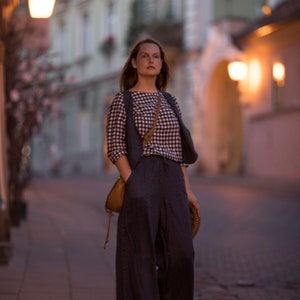 Charcoal linen wide-leg trousers worn on model, full-length three-quarter view; high-rise waistline, wide flowing legs, soft vertical folds, side pocket with hand inside, hem near the ground; evening city sidewalk.