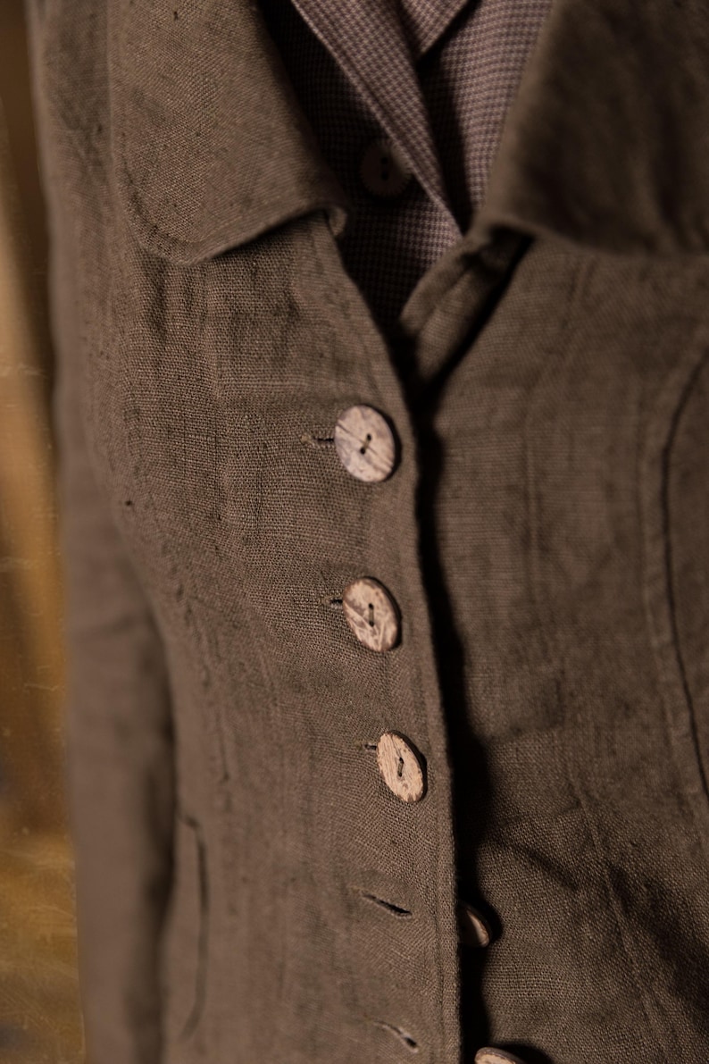 Close-up of mushroom brown slim fit linen jacket on model, showing curved collar, fitted seams and four coconut buttons over checked linen dress, retro buttoned linen jacket by knock knock linen.