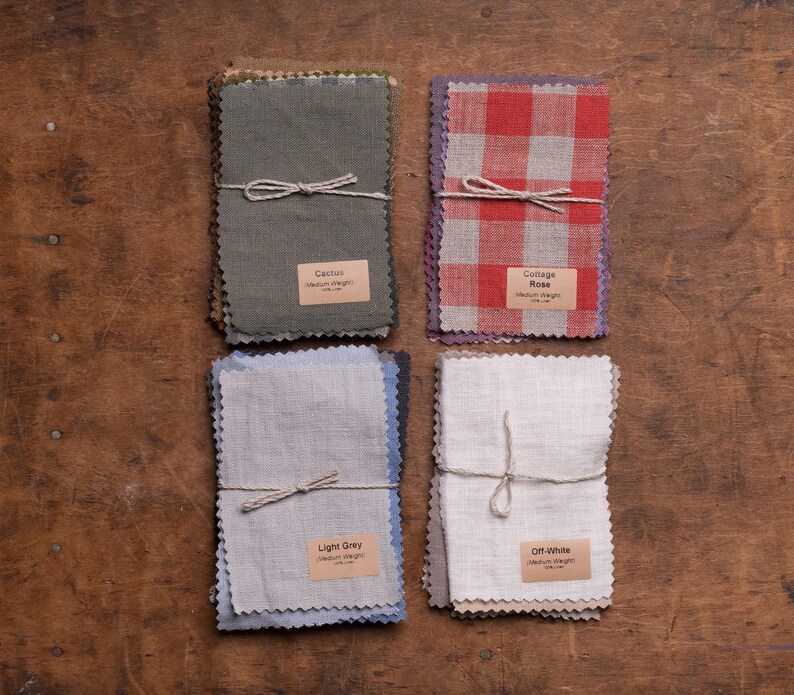 KnockKnockLinen fabric samples—four bundles of medium-weight linen swatches tied with string: Cactus green, Cottage Rose red-white gingham, Light Grey, and Off-White; pinked edges, labeled, arranged in a flat lay on a wooden table.