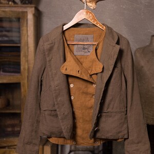 SPARROW linen vest in brown, displayed on a hanger in a front-view full-length photo, with double rows of light buttons, a curved front flap, a straight lower edge, and an open brown jacket with long sleeves over it, Knock Knock Linen.
