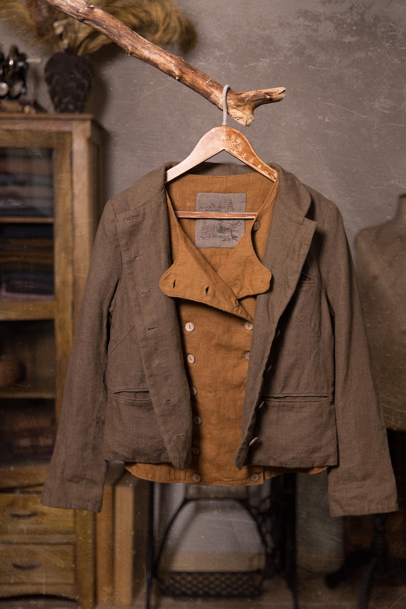 SPARROW linen vest in brown, displayed on a hanger in a front-view full-length photo, with double rows of light buttons, a curved front flap, a straight lower edge, and an open brown jacket with long sleeves over it, Knock Knock Linen.