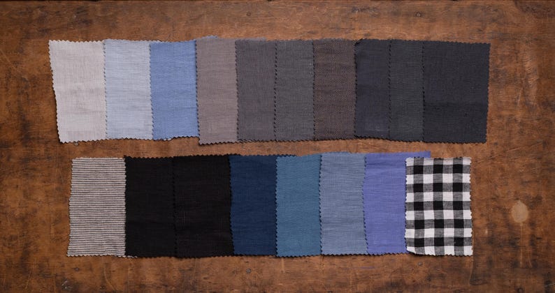 Linen fabric samples in pale gray, light blue, taupe, charcoal, navy, and black displayed in a flat lay close-up, set in two rows on a brown wooden surface, with zigzag-cut edges, rectangular pieces, a striped swatch, and a checked swatch.