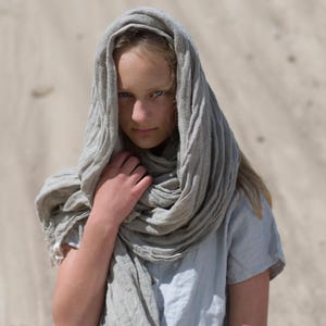 KnockKnockLinen short-sleeve linen top “Silence” — light grey, round neck, loose fit — shown on model outdoors with an oversized natural-flax linen scarf wrapped over head and neck against a sandy backdrop. Linen blouse / linen top.