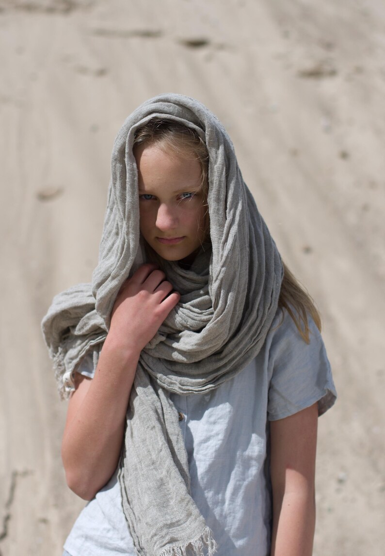 KnockKnockLinen short-sleeve linen top “Silence” — light grey, round neck, loose fit — shown on model outdoors with an oversized natural-flax linen scarf wrapped over head and neck against a sandy backdrop. Linen blouse / linen top.