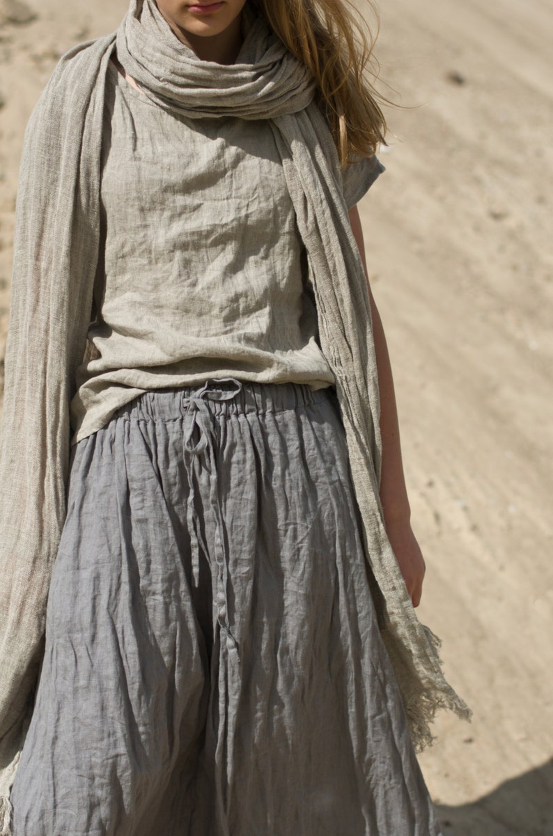 Model standing on sand wearing frost grey linen drawstring pants with loose fit, paired with matching short-sleeved top and scarf; fabric appears soft and naturally wrinkled. Keywords: linen summer pants, drawstring pants, loose fit.