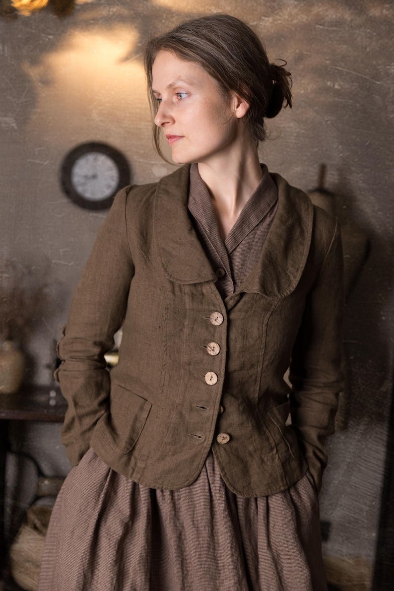 Close-up of woman wearing slim fit mushroom brown linen jacket with curved collar, button front and pockets over brown dress, shown on model in rustic studio, retro buttoned linen jacket blazer by knock knock linen.