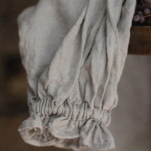 Close-up detail of one natural linen smock dress sleeve, showing the puff sleeve shape and ruffled elastic cuff.