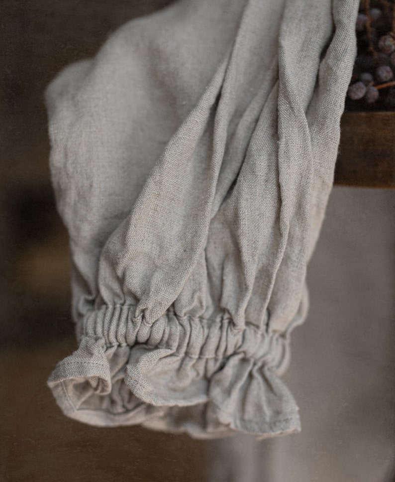 Close-up detail of one natural linen smock dress sleeve, showing the puff sleeve shape and ruffled elastic cuff.