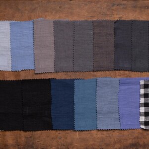 KnockKnockLinen fabric samples—20 linen swatches in gray, blue, and black tones, plus stripe and black-white gingham; pinked edges in two rows, flat lay on a wooden table. Fabric swatch book for linen fabric.