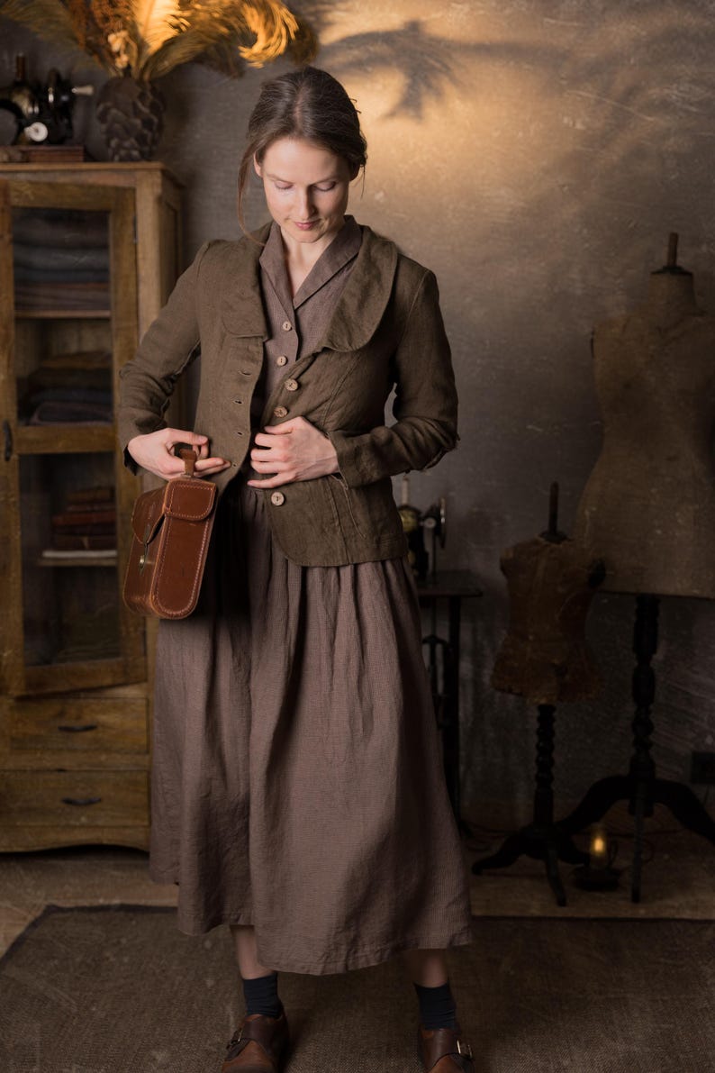 Woman wearing slim-fit mushroom brown linen jacket with button front, curved collar and long sleeves, styled over brown midi dress and holding leather bag in rustic studio, retro linen jacket by knock knock linen.