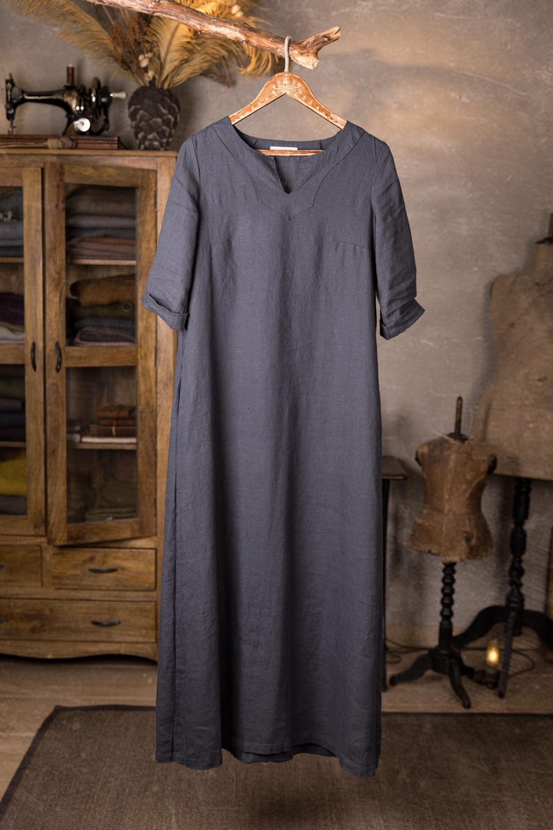 linen dress hanging on hanger from a branch, front view full-length crop, V-slit neckline, short yoke seam lines at chest, elbow-length sleeves with turned cuffs, plain front panel, straight hem; vintage cabinet and mannequin in background, knockknocklinen.