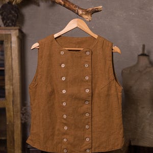 SPARROW linen vest in brown, displayed on a hanger in a front-view full-length photo, with a round neckline, sleeveless armholes, double rows of light buttons, an offset front panel, and a slightly curved hem, Knock Knock Linen.