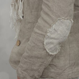 Side close-up of natural herringbone linen jacket with raw oval elbow patch, long sleeve, pocket and wooden button, worn with matching linen pants and scarf on model, vintage style women’s linen jacket by knock knock linen.