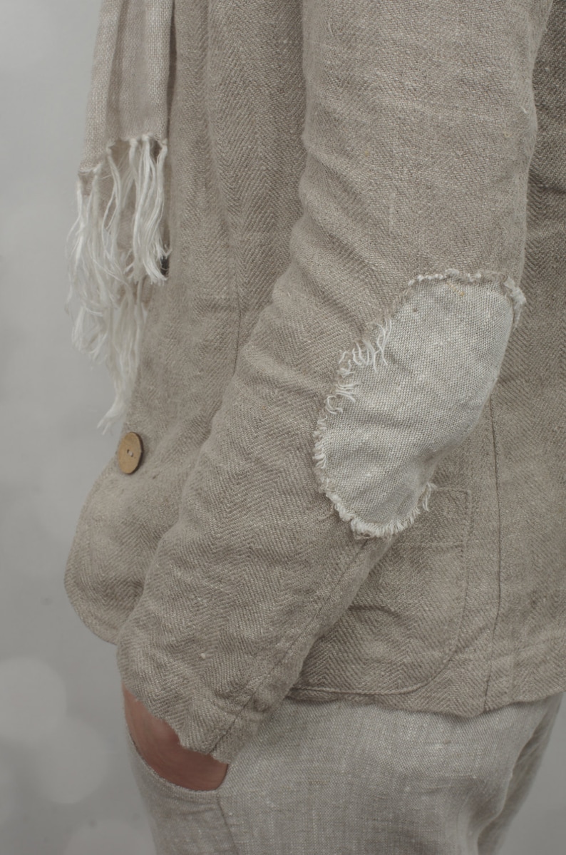 Side close-up of natural herringbone linen jacket with raw oval elbow patch, long sleeve, pocket and wooden button, worn with matching linen pants and scarf on model, vintage style women’s linen jacket by knock knock linen.