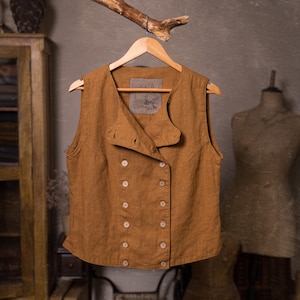 SPARROW linen vest in brown, displayed on a hanger in a front-view full-length photo, with a round neckline, sleeveless armholes, double rows of light buttons, an offset front panel, and a slightly curved hem, Knock Knock Linen.