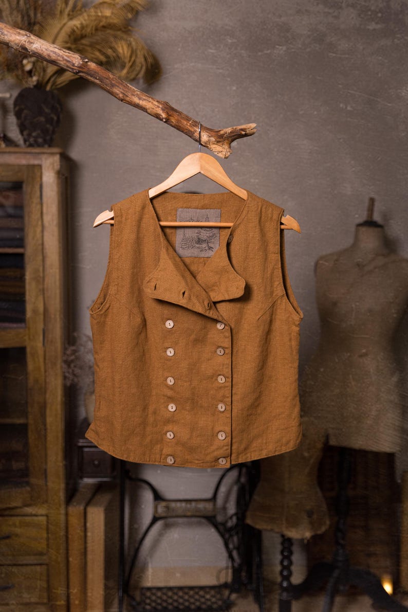 SPARROW linen vest in brown, displayed on a hanger in a front-view full-length photo, with a round neckline, sleeveless armholes, double rows of light buttons, an offset front panel, and a slightly curved hem, Knock Knock Linen.