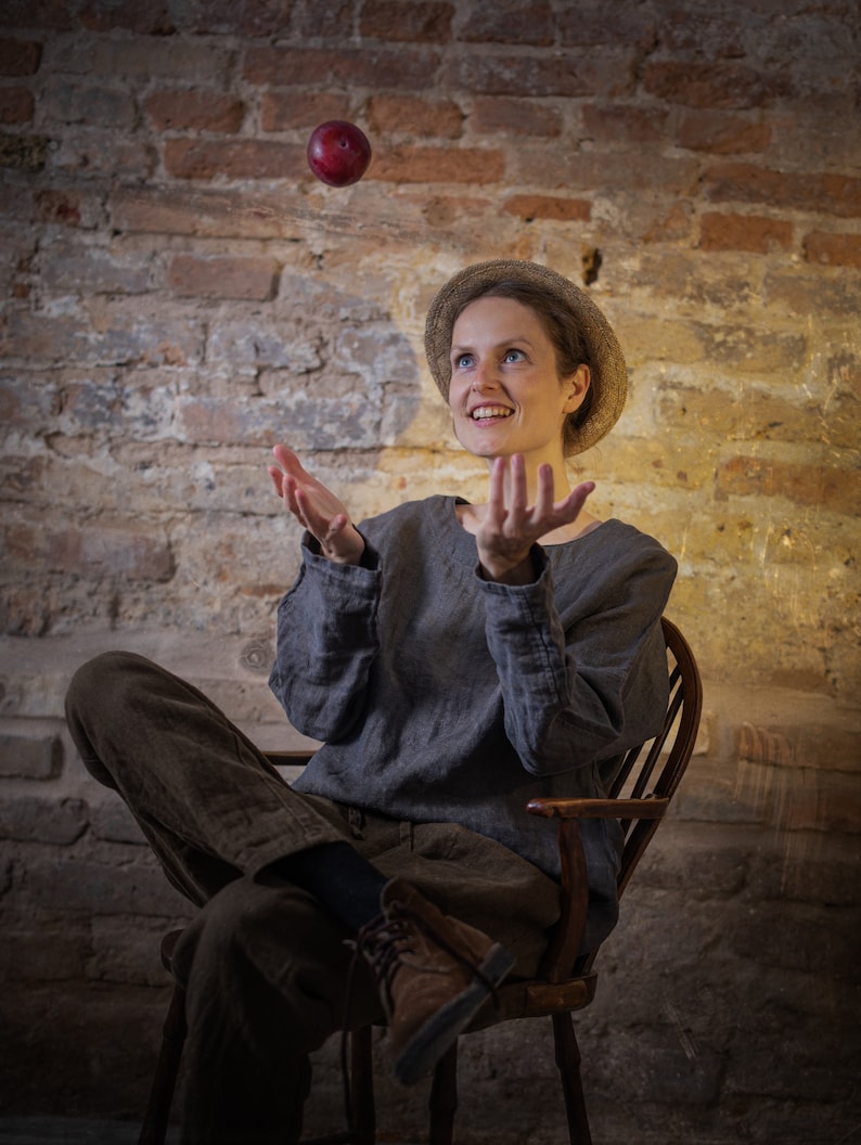 Linen pants in dark brown, shown on a seated model in a full-length three-quarter view, with a gathered waistband, visible drawstring ties, loose tapered legs, softly wrinkled fabric, and brown lace-up shoes, Knock Knock Linen.