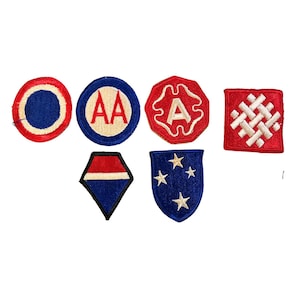 Op de afbeelding: Een verzameling van zeven vintage militaire patches in verschillende vormen. De patches hebben rode, blauwe en witte kleuren, met ontwerpen zoals sterren, letters en geometrische patronen. Deze patches zijn waarschijnlijk afkomstig van een militair uniform.