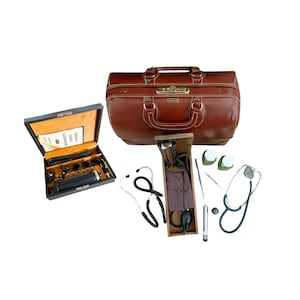 Może przedstawiać: Brązowa skórzana torba lekarska z uchwytem, otwarta, aby odsłonić instrumenty medyczne. Czarna walizka z narzędziami medycznymi jest otwarta po lewej stronie. Widoczne są dwa stetoskopy i inne materiały medyczne.