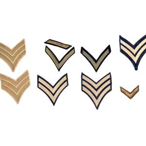 May include: A collection of various military rank insignia patches. The patches are in a chevron shape, with colors including tan, olive green, and navy blue. Some have multiple stripes, while others have a single stripe.