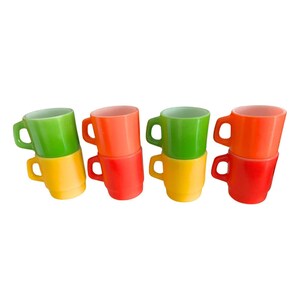 May include: A collection of six colorful vintage mugs in shades of green, orange, red, and yellow. Each mug is stacked on top of another, creating a vibrant display. The mugs have a classic design with a handle.
