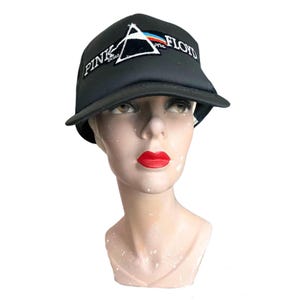 Może przedstawiać: Czarna czapka bejsbolowa z logo Pink Floyd, białym trójkątem z tęczowym spektrum. Nazwa zespołu jest wyhaftowana na czapce na biało. Czapka jest prezentowana na głowie manekina.