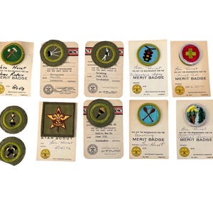 Op de afbeelding: Een verzameling vintage Boy Scout-verdienstenbadges en -patches. De badges hebben verschillende ontwerpen, waaronder een hamer, een ster, een verkeerslicht en een kruis. Elke badge wordt vergezeld van een kaart met tekst, inclusief de naam "Lou Hurst".