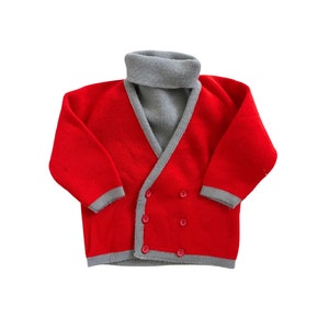 May include: A red cardigan with a grey turtleneck collar and four buttons. The cardigan has grey trim around the edges of the sleeves and the bottom.