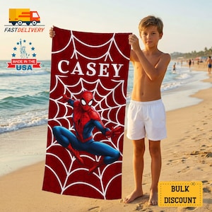 May include: A red beach towel featuring a white spiderweb design and a graphic of Spider-Man in action. The name "CASEY" is printed in large white letters. The towel is made in the USA.