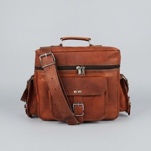 May include: A brown leather satchel bag featuring a top handle, an adjustable shoulder strap with a silver buckle, a zipped main compartment, and a front pocket secured with a buckle and two silver rivets, plus two side pockets with flaps.