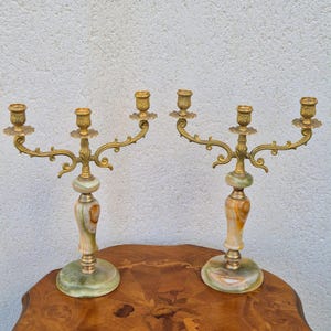 Peut inclure: Une paire de candélabres à trois branches dotés de bras et de bobèches en métal doré orné, reposant sur des bases cylindriques lisses en pierre rubanée verte et ambre avec des socles circulaires et des accents en métal doré.