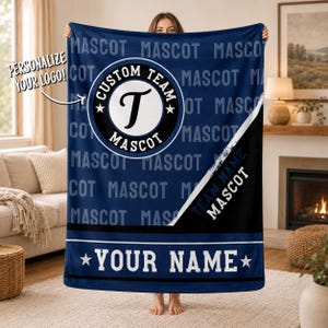 Könnte beinhalten: Eine dunkelblaue Fleecedecke mit wiederholtem MASCOT-Muster, einem zentralen kreisförmigen Logo mit dem Buchstaben T, dem Text CUSTOM TEAM MASCOT, einem diagonalen schwarzen Streifen mit TEAM NAME MASCOT und einem unteren Banner mit dem Text YOUR NAME.