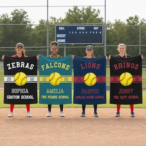 May include: Four softball team banners in black, teal, navy, and maroon. Each banner displays a team name, a softball graphic, the numbers 20 and 26, a player's name, and a school name. The background includes a scoreboard and trees.